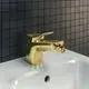 Goldfarbene Bidetarmatur von Ideal Standard mit schmalem Auslauf und Hebel für die Wasserregulierung. Dazu weiße Waschfläche und Kacheln in Schwarz.